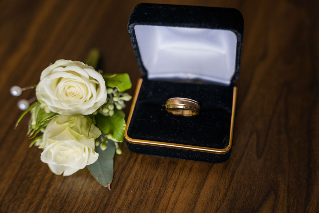 boutonniere and man's wedding ring sitting on a wooden table