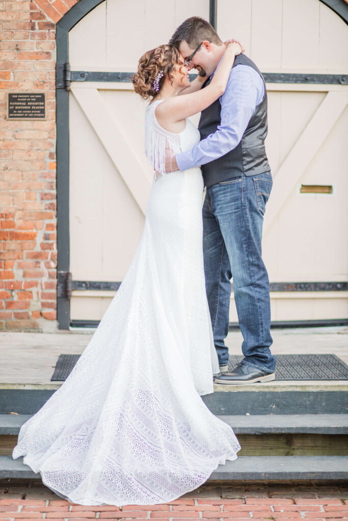 bride and groom stand facing and hugging each other on the stairs of shuey mill