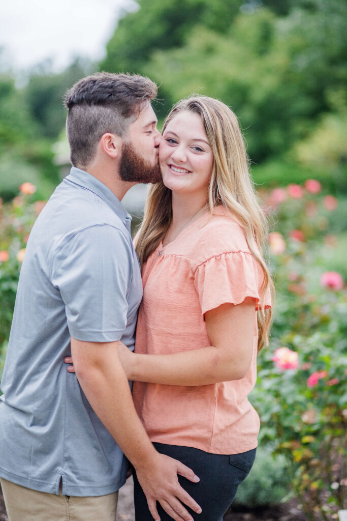 man kissing the cheek of his girlfriend while they get engagement pictures at ault park