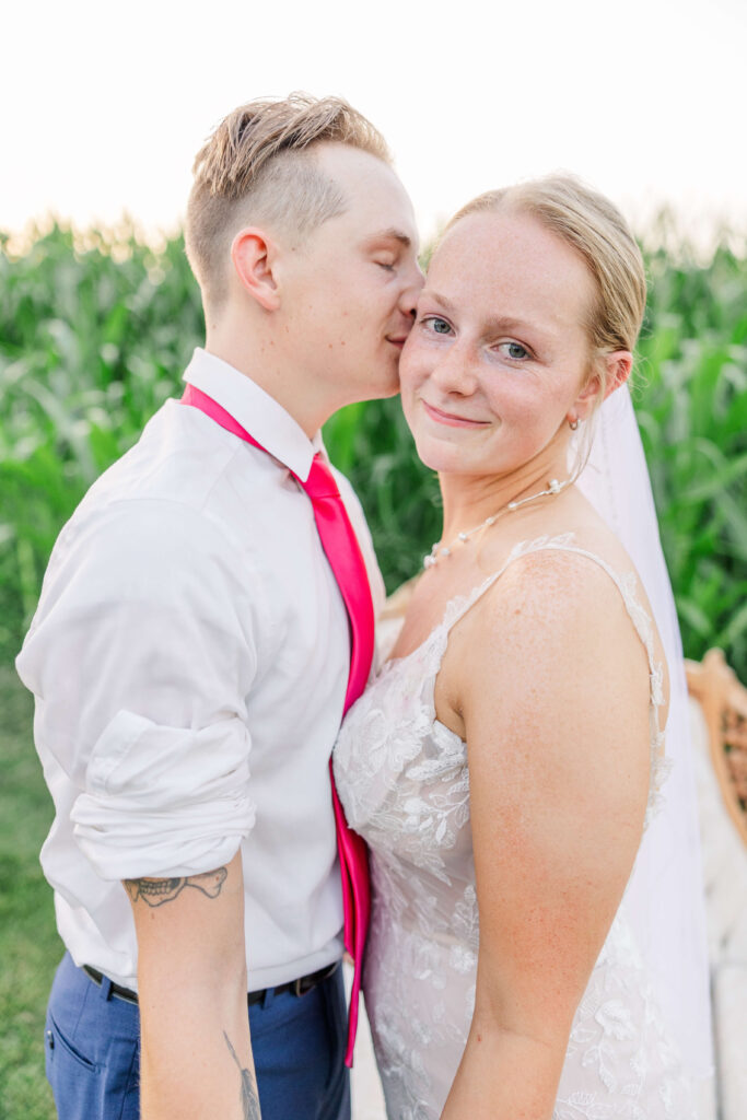 groom kissing the cheek of his bride at the white barn venue