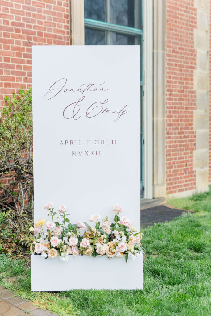 a wedding sign with florals on the bottom outside of peterloon estate