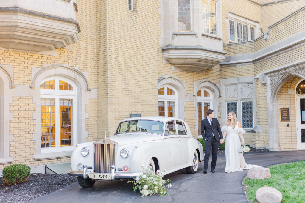 A bride and groom stand outside laurel hall, a wedding venue. A rolls royce is parked next to them. 