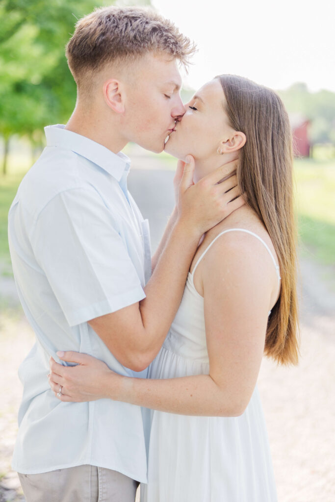 A man and woman kiss at hidden valley orchards. She is wearing a white dress and he is wearing a light blue shirt. 